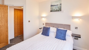 A bedroom with a large bed, two wall-mounted lights, a painting above the bed, and a wooden door.