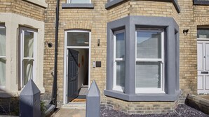 A corner bay window with a dark frame, a door with a '5' number plate, and a small garden area with gravel.