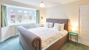 Ein Schlafzimmer mit einem großen Bett, einem Fenster mit Vorhängen, einem Heizkörper, einem Nachttisch mit Lampe und einer Tür.
