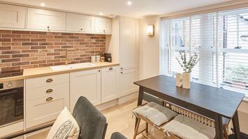 A modern kitchen with a brick backsplash, white cabinetry, and a dining area with a bench and table.