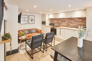 Une cuisine moderne avec des meubles blancs, un mur de fond en briques et un coin repas comprenant une table et des chaises.