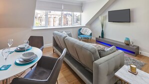 Een moderne woonkamer met een bank, eettafel en een aan de muur bevestigde televisie.