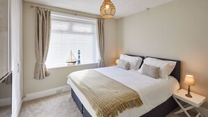 A bedroom with a bed, bedside table, lamp, curtains, and a window with blinds. - Host Stay Seagull Cottage (Bridlington)