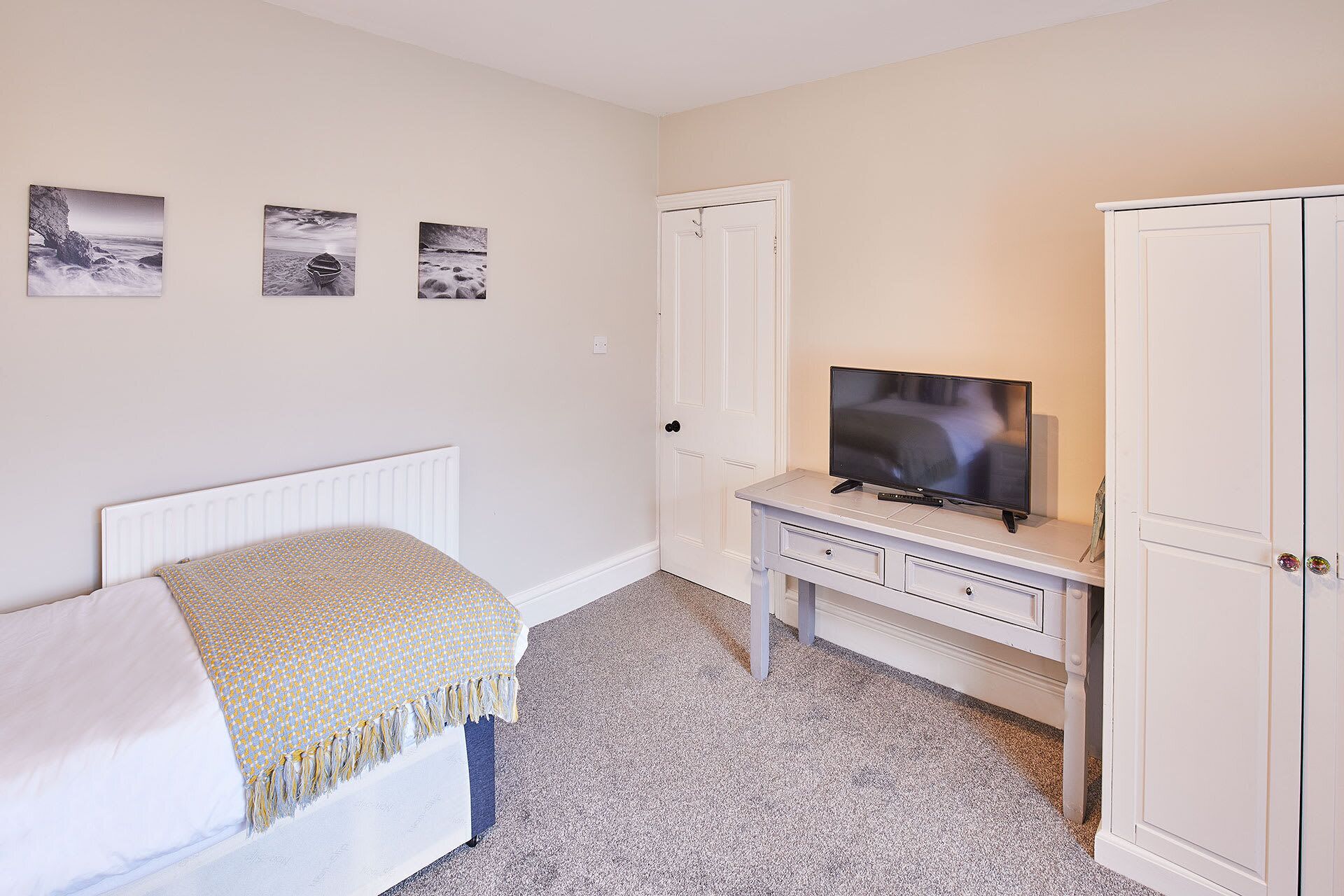 A bedroom with a bed, a TV on a dresser, and three framed pictures on the wall.