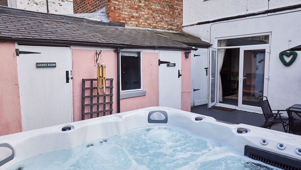 A hot tub in a backyard with a pink and white building, a bar, and a games room. - Host Stay Seagull Cottage (Bridlington)