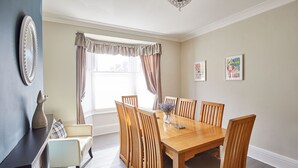 A dining area with a wooden table and six chairs, a vase with flowers, and two framed pictures on the wall. - Host Stay Seagull Cottage (Bridlington)