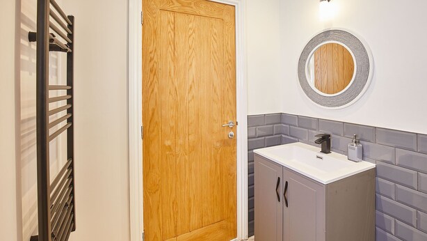 Une salle de bain avec une porte en bois, un miroir rond, un lavabo doté d’un robinet moderne et un porte-serviettes.
