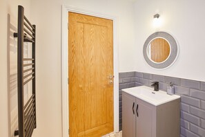 Bathroom features a vanity with a white countertop and black faucet, a round mirror, and gray tile walls.