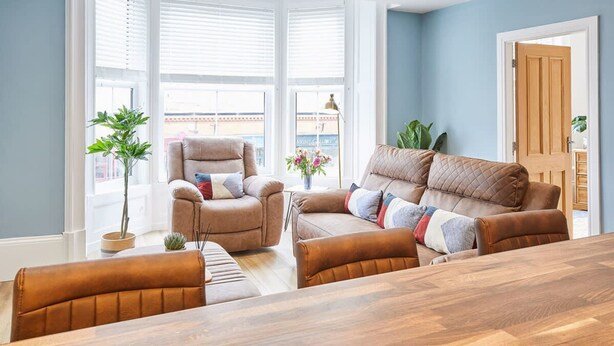 A living room with a sofa, armchairs, a dining table, and large windows. - Host Stay The Seaside Escape (Saltburn-by-the-Sea)
