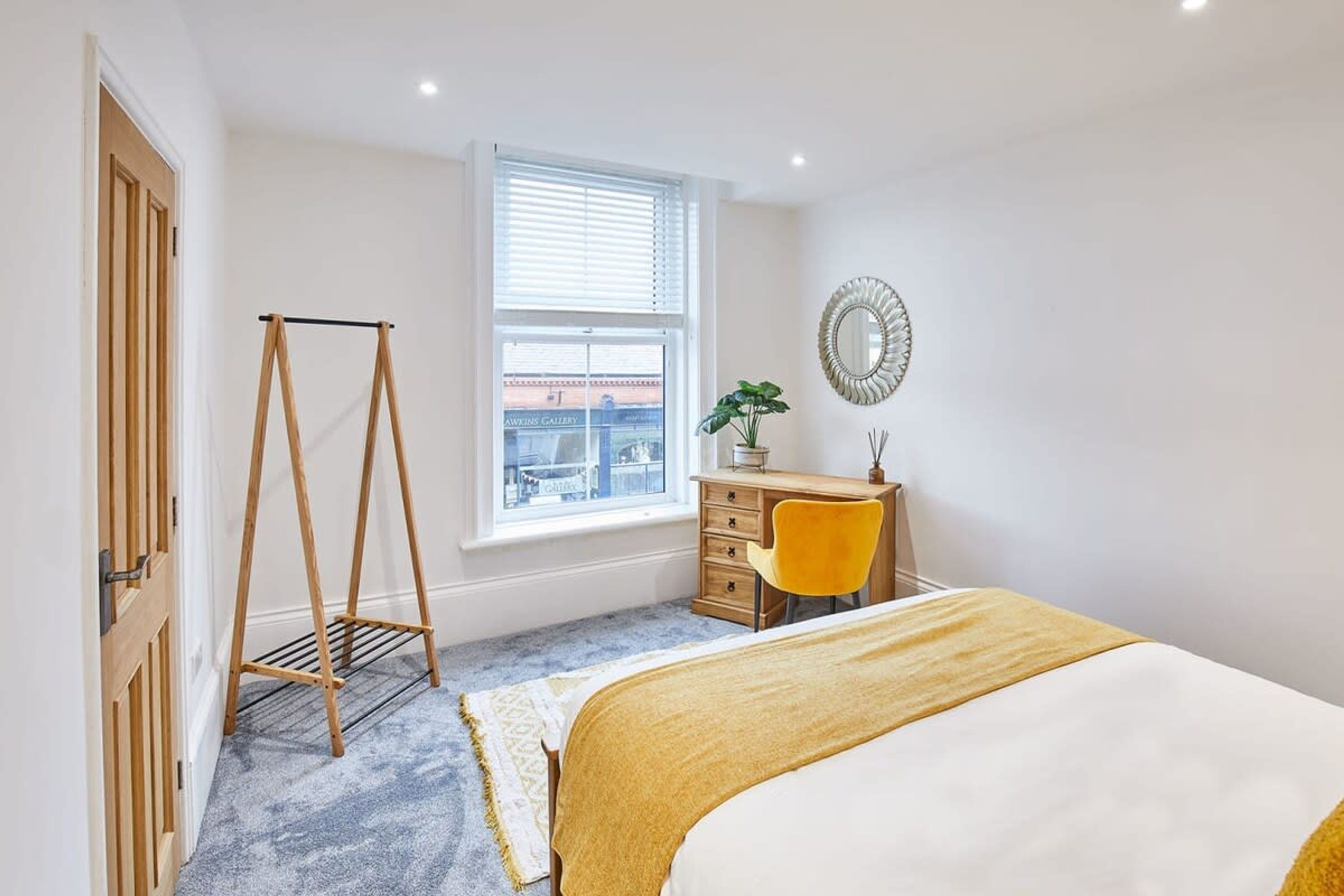 A bedroom with a bed, a desk, a chair, a window, and a door.