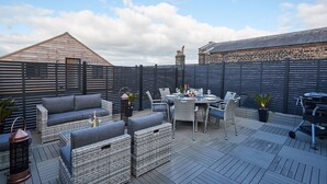 Une terrasse extérieure aménagée avec des meubles en osier, une table dressée pour le repas et un barbecue.