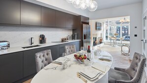 Une cuisine moderne avec des meubles de couleur sombre, un plan de travail en marbre et un coin repas avec une table en marbre, mise pour quatre personnes.