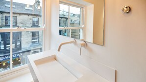 Une salle de bain blanche avec une grande fenêtre, un lavabo blanc et un miroir.