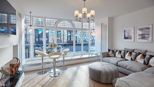 Un salon moderne avec une grande fenêtre, un lustre, un canapé et une table basse en verre.