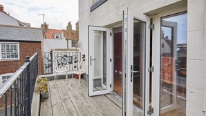A balcony with a wooden floor, a metal railing, and a white chair. - Host Stay One Mulgrave Place (Whitby)