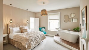 A bedroom with a large bed, a sitting area with a chair, a bathtub, and a window with blinds. - Host Stay One Mulgrave Place (Whitby)