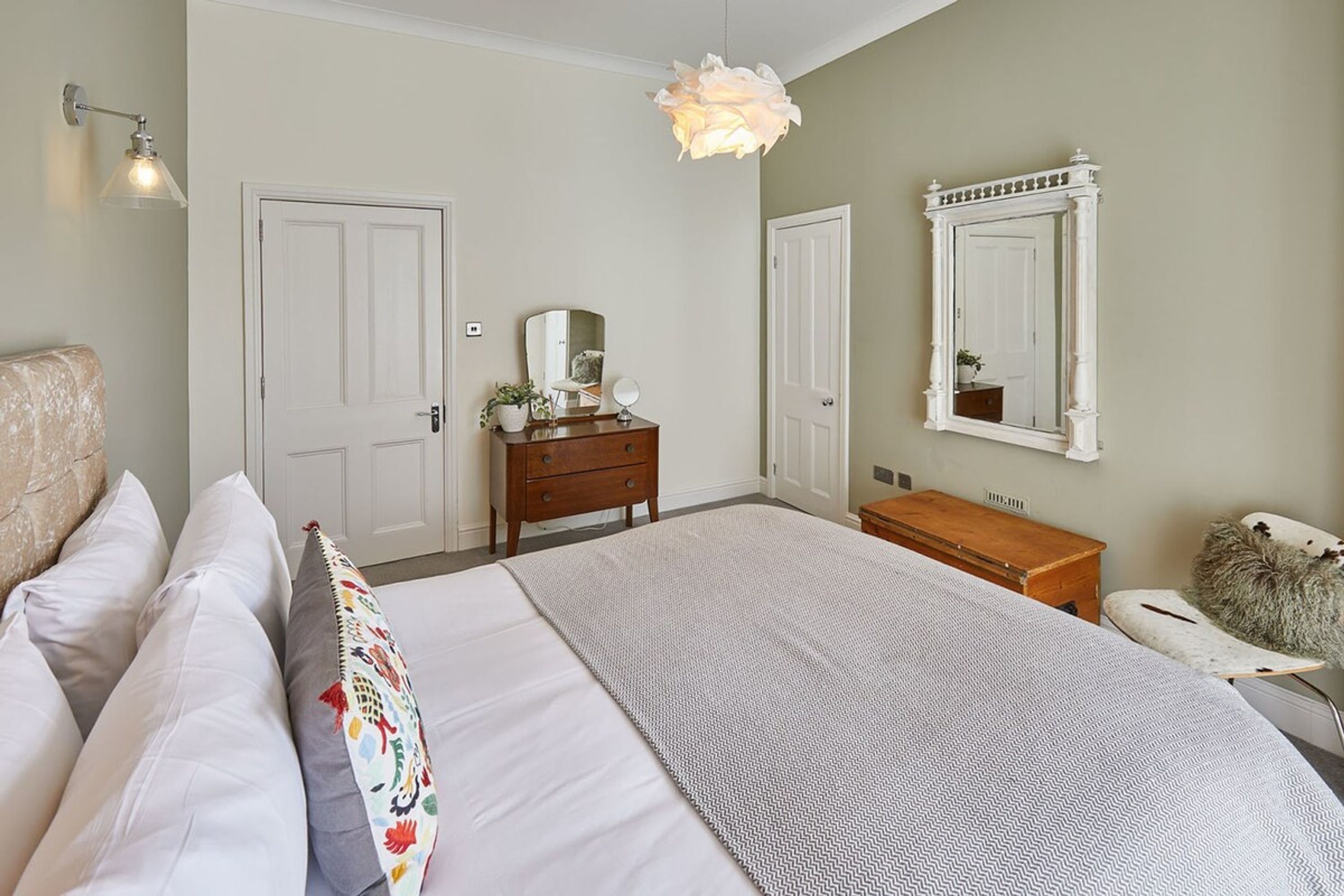 Une chambre à coucher avec un grand lit, deux portes, une commode, un miroir et un luminaire suspendu.