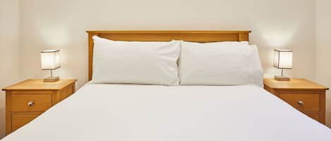 A neatly made bed with a wooden headboard, flanked by two bedside tables with lamps.