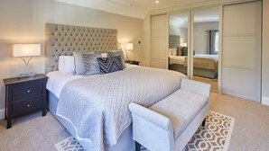 Ein Schlafzimmer mit einem großen Bett, einem Nachttisch, einer Bank, einem Kleiderschrank und einem Spiegel.