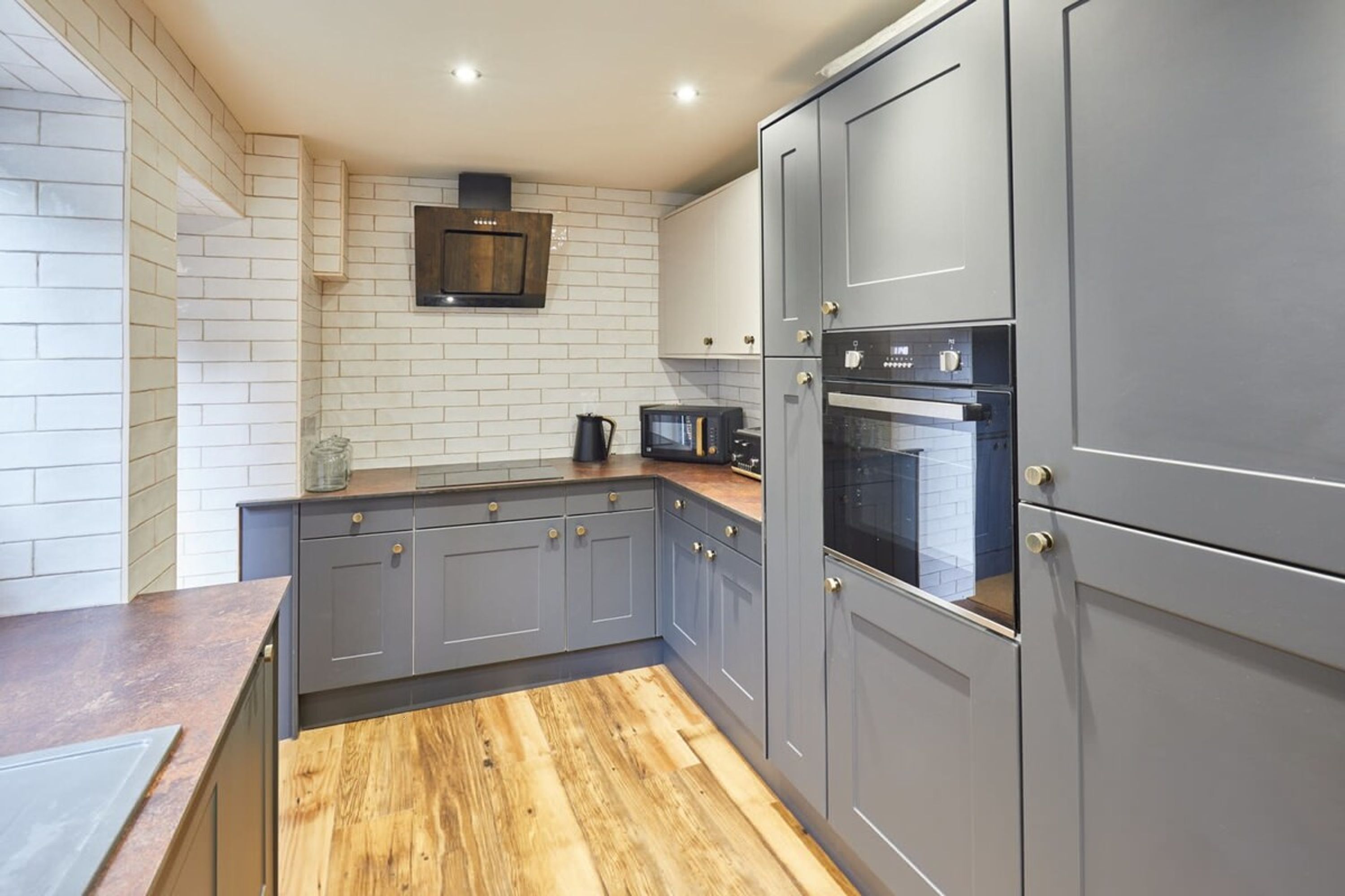 A modern kitchen with grey cabinets, a wooden countertop, a microwave, and an oven.