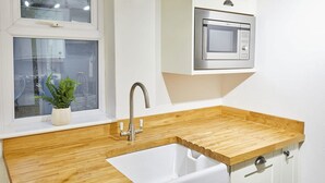 A kitchen with a wooden countertop, a white sink, a stainless steel faucet, a potted plant, and a microwave above the countertop.