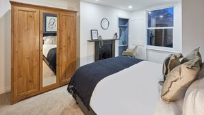 A bedroom with a large bed, a wardrobe with a mirror, a fireplace, and a window with a view of the outside.