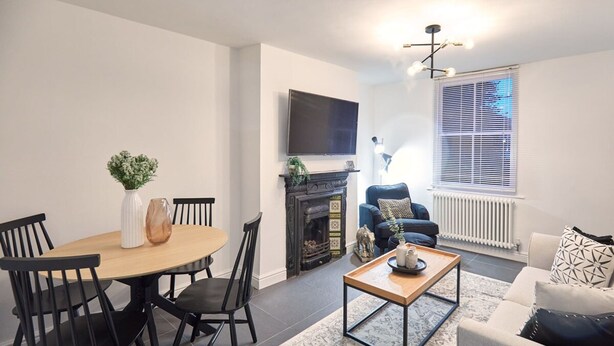 A modern living room with a fireplace, a television mounted on the wall, and a dining area with a table and chairs.