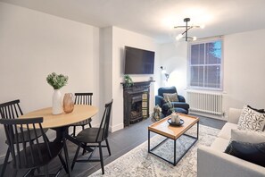 A modern living room with a fireplace, a television mounted on the wall, and a dining area with a table and chairs. - Host Stay High Street Cottage (Stockton-on-Tees)