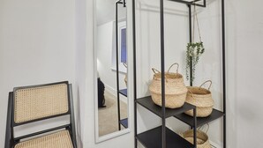 A room with a black metal shelving unit holding woven baskets and a hanging plant. A rattan chair is positioned to the left.