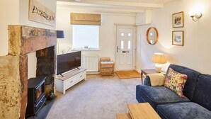 A cozy living room with a fireplace, a television, a sofa, and a door leading to another room. - Host Stay Waterlily Cottage (Middlesbrough)