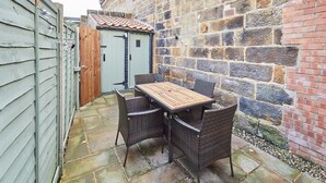 A patio with a table and chairs, a wooden door, and a stone wall. - Host Stay Waterlily Cottage (Middlesbrough)