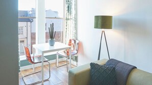 Ein modernes Wohnzimmer mit einer Couch, einem Tisch und Stühlen. Es gibt ein Fenster mit Vorhängen, eine Stehlampe und einen Ausblick nach draußen.