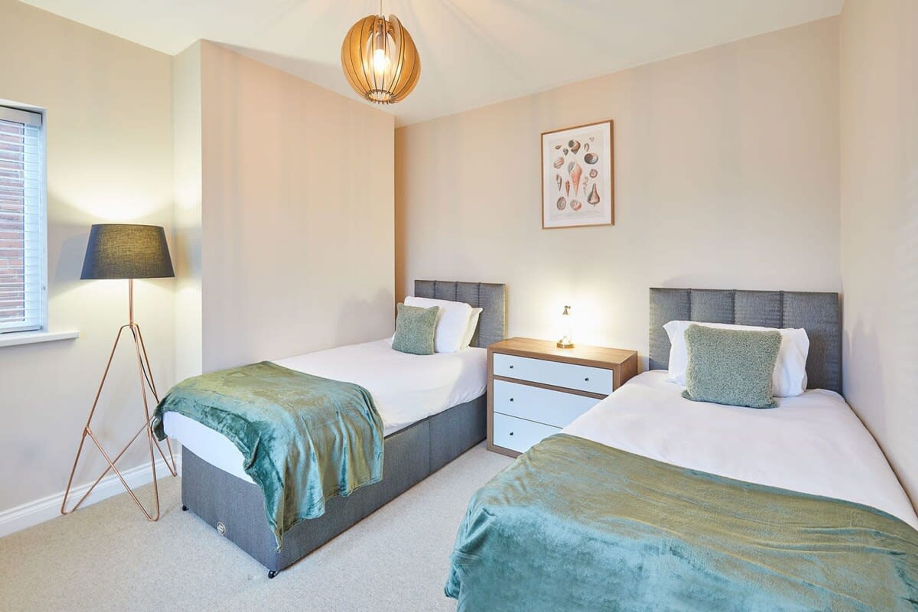 A bedroom with two beds, a bedside table, a lamp, and a framed picture on the wall.