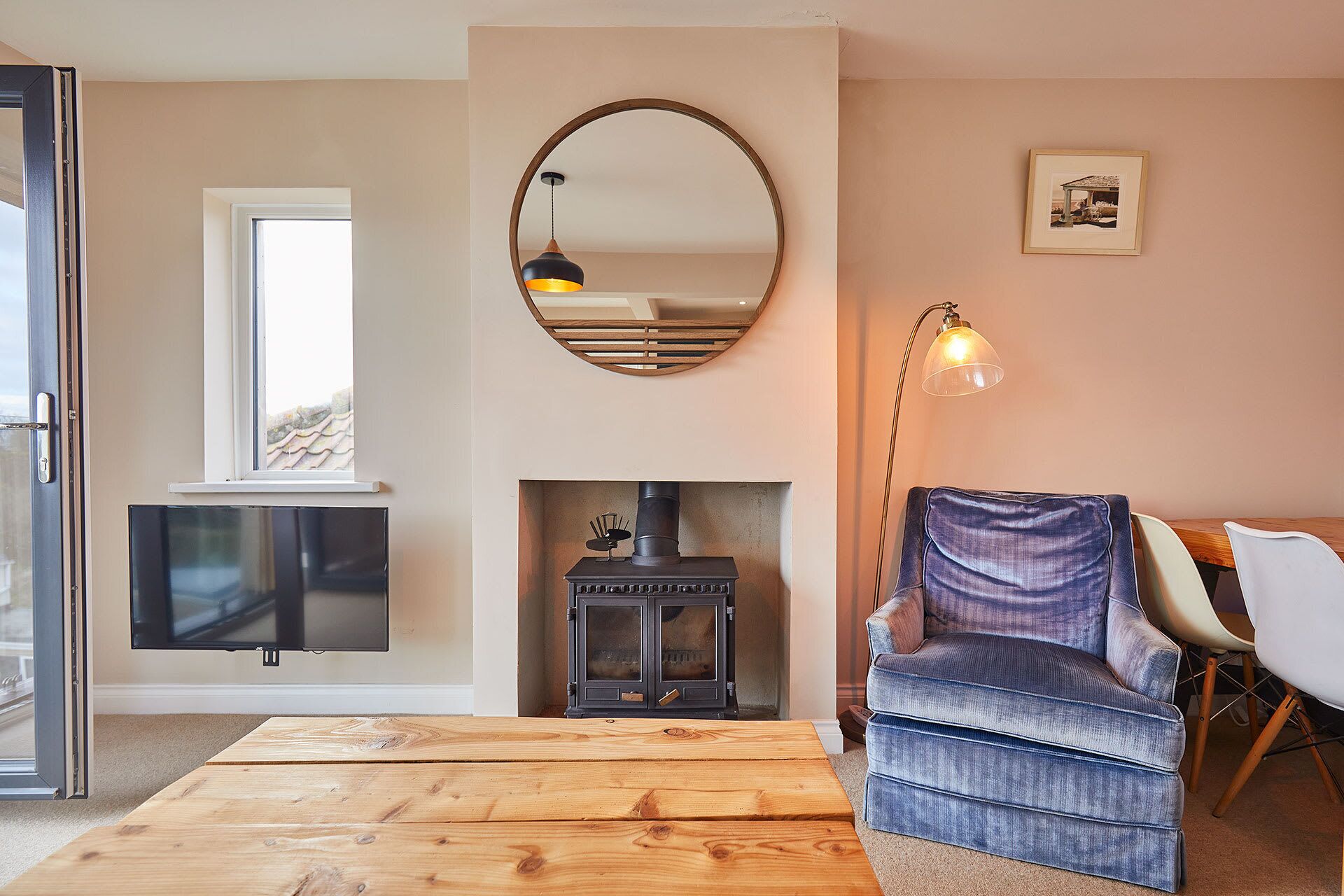 Una sala de estar con chimenea, televisor, una mesa de centro de madera y un sillón azul.