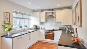 A modern kitchen with white cabinets, a black countertop, and a wooden floor. - Host Stay Newsam Crescent (Stockton-on-Tees)
