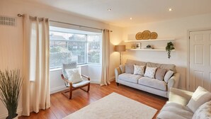 A living room with a sofa, a chair, a floor lamp, and a large window with curtains. - Host Stay Newsam Crescent (Stockton-on-Tees)