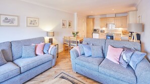 Ein modernes Wohnzimmer mit zwei grauen Sofas, einem Esstisch und einer Küche im Hintergrund.