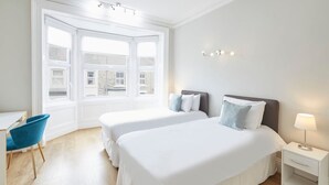A hotel room with two beds, a desk, a chair, and a window with a view of buildings. - Host Stay Victorian Seahouse (Saltburn-by-the-Sea)