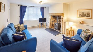 A living room with a stone fireplace, blue sofas, and a television. - Host Stay Kenmore (Corbridge)