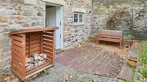 A stone building with a wooden bench and a firewood storage area. - Host Stay Kenmore (Corbridge)