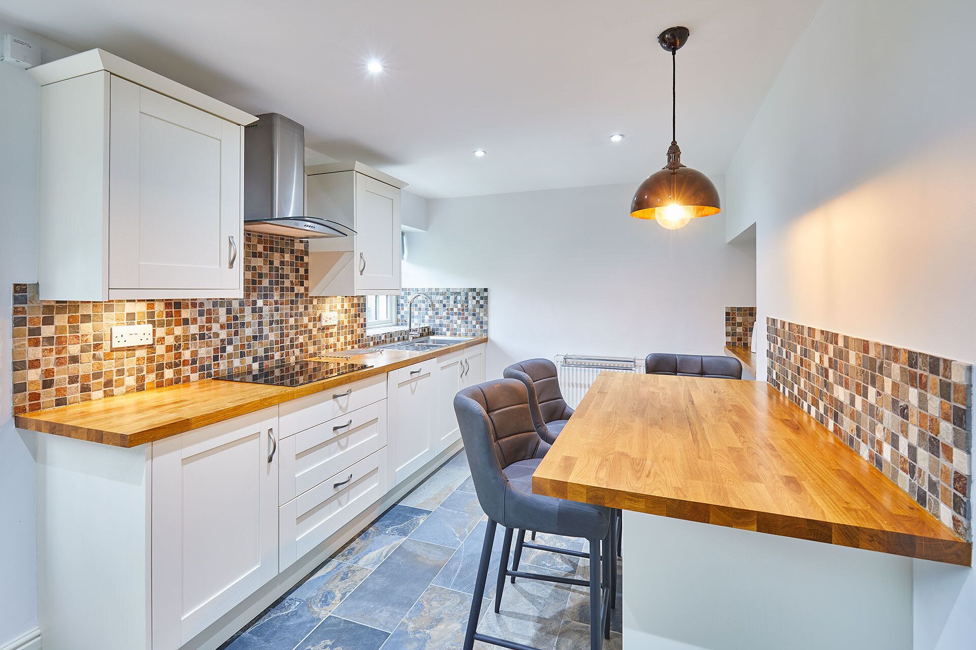 A modern kitchen with white cabinets, a wooden countertop, and a tiled backsplash.