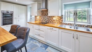 A modern kitchen with white cabinets, a built-in oven, a tiled backsplash, and a window with a view of the outdoors. - Host Stay Kenmore (Corbridge)