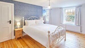 A bedroom with a bed, wooden floor, a nightstand, a lamp, a window with curtains, and a radiator. - Host Stay Kenmore (Corbridge)