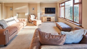 A spacious living room with a large TV, comfortable seating, and a view of the outdoors. - Host Stay The Chimneys (Alnwick)