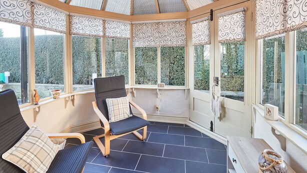A sunroom with a high ceiling, patterned curtains, and a chair with a cushion. - Host Stay The Chimneys (Alnwick)