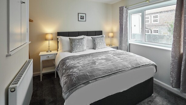A bedroom with a bed, bedside tables, a radiator, a window with curtains, and a picture on the wall.