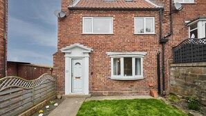A two-story brick house with a white front door, a bay window, and a small front garden.