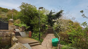 A stone staircase leading up a hill, surrounded by lush greenery and a metal fence.