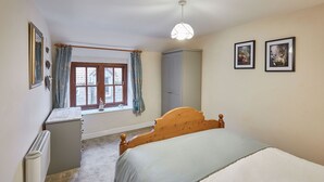 Un dormitorio con cama, ventana con cortinas, armario y dos cuadros en la pared.