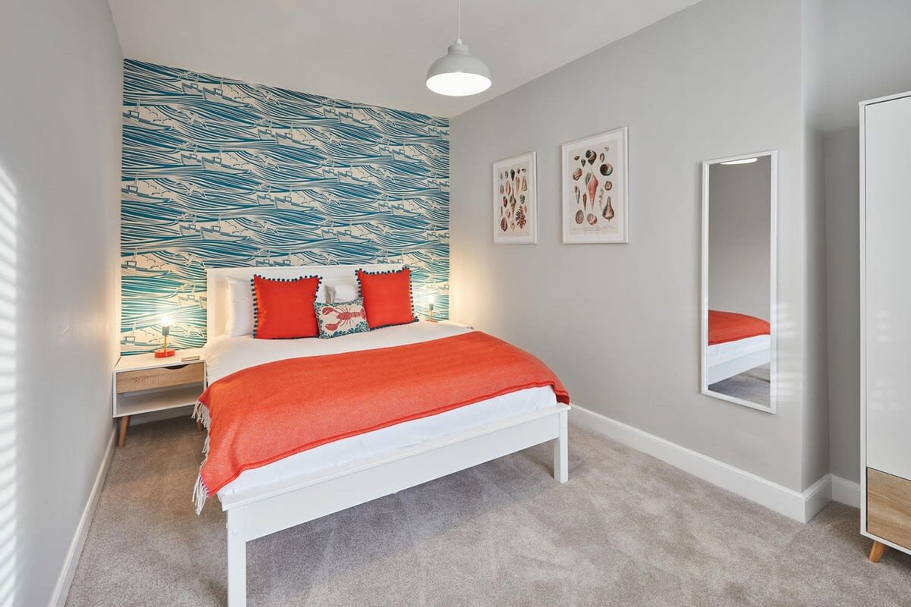 A bedroom with a bed, a nightstand, a wall with a blue and white pattern, and a mirror.